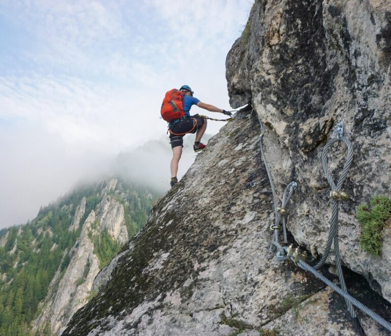 stunning-shot-young-man-climbing-up-cliff-cold-foggy-day_181624-18833